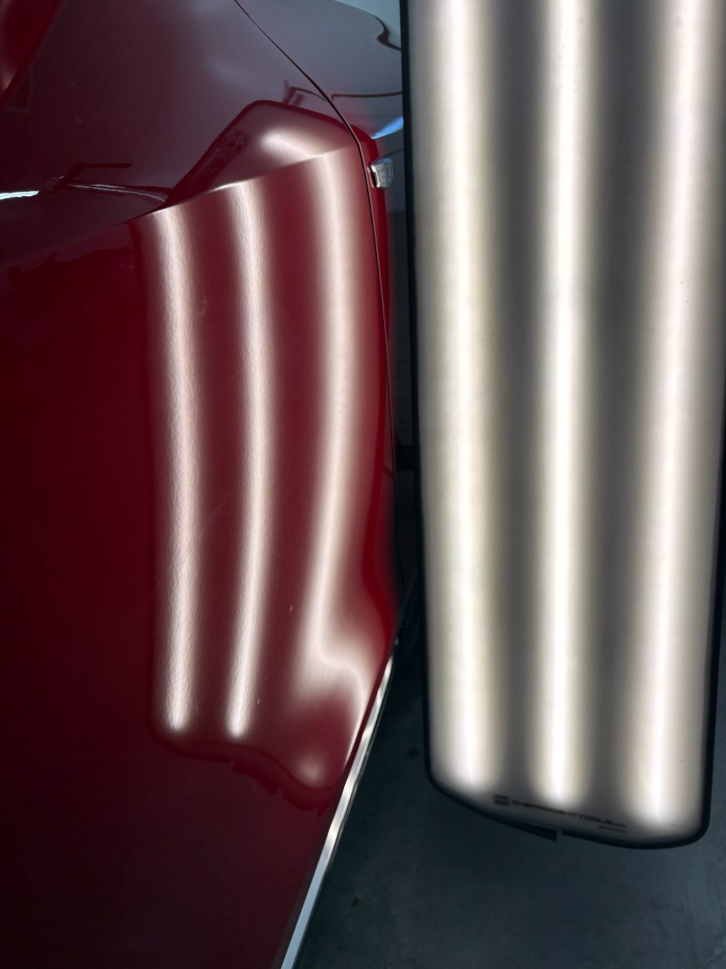 Reflection lines bending over a dent in a red Cadillac panel before paintless dent repair